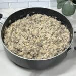 A steaming skillet filled with seasoned ground beef, tender rice, and mushrooms, bell pepper, onion, garlic and seasonings.