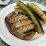 A side of Baked Parmesan Zucchini served with a grilled pork chop.