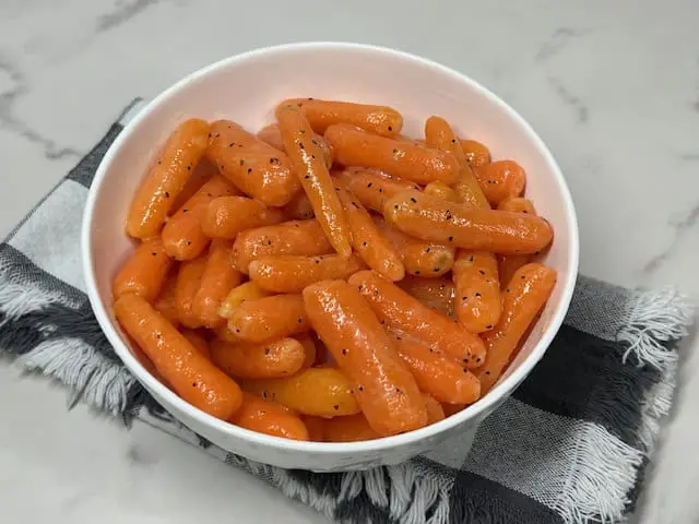 A bowl of bright, tender, buttered carrots and garnished with fresh parsley.