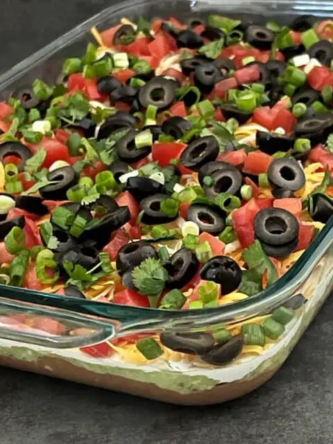 Classic Seven Layer Dip is a yummy appetizer for any get-together. This dip is filled with delicious ingredients and is easy to make. #SuperBowl #PartyFood #ClassicRecipes #7LayerDipRecipe #LayeredDip 