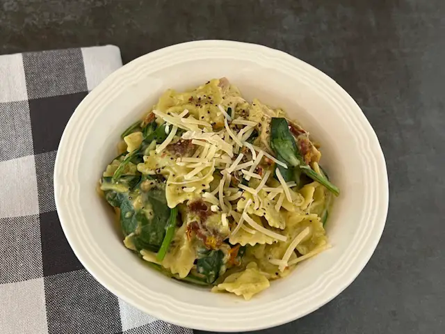 A close-up of creamy basil pesto chicken pasta with parmesan cheese and freshly cracked pepper in a bowl.