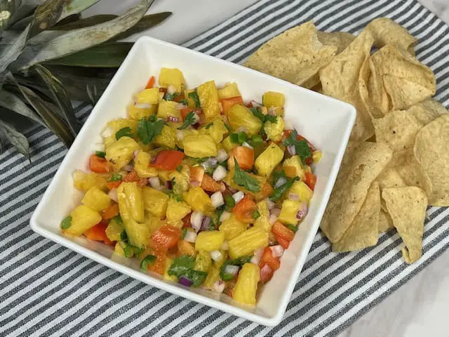 A colorful bowl of fresh pineapple salsa with diced pineapple, red onion, red bell pepper, and cilantro, ready to be served with tortilla chips.
