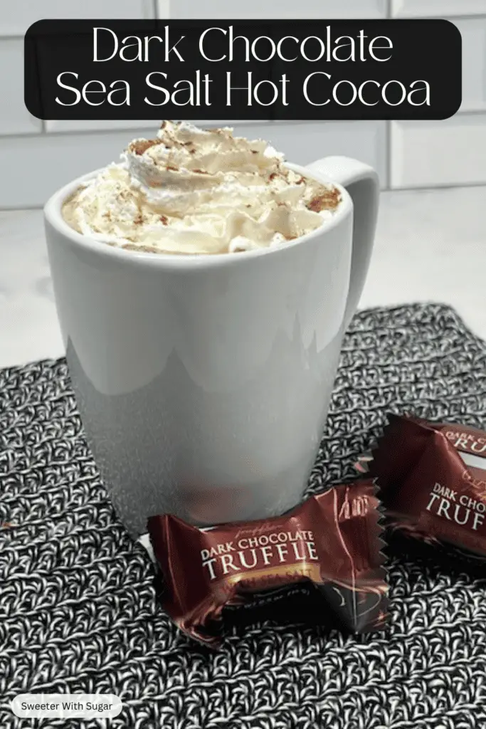 A steaming mug of dark chocolate sea salt hot cocoa, topped with whipped cream and sprinkled with flaky sea salt and cinnamon.