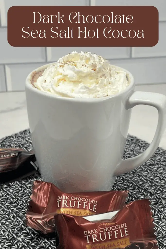A steaming mug of dark chocolate sea salt hot cocoa, topped with whipped cream and sprinkled with flaky sea salt and cinnamon.