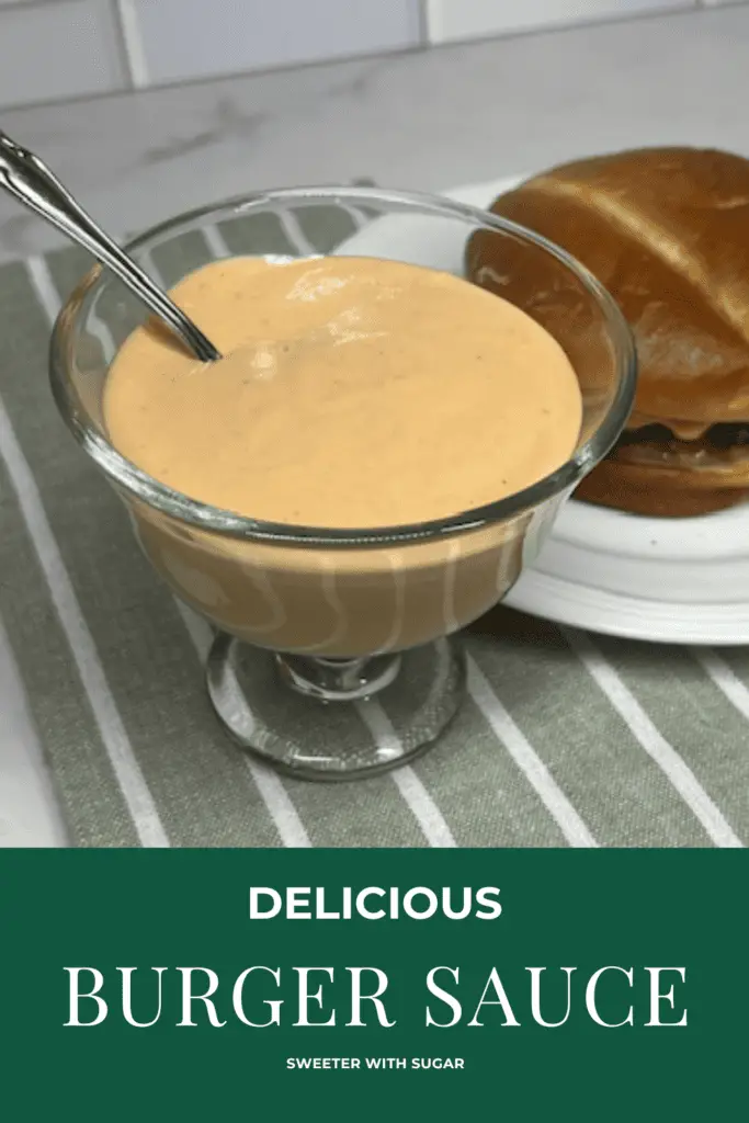 A small bowl of creamy homemade burger sauce with a spoon, surrounded by burger ingredients like lettuce, tomato, and pickles. #BurgerSauce #HomemadeSauce #EasyRecipe #SecretSauce #BurgerLover #SauceRecipe #GrillSeason