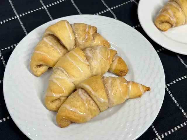 A plate of golden brown cinnamon sugar crescent rolls, filled with a buttery cinnamon and sugar filling and with a drizzle of vanilla glaze on top.