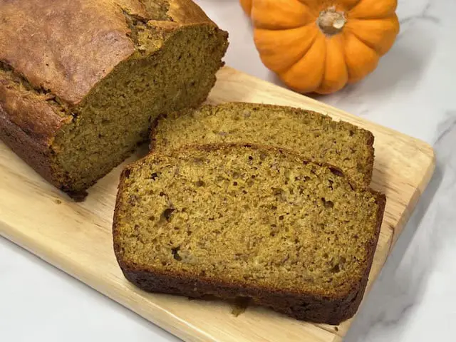 A moist and fluffy loaf of pumpkin banana bread sliced on a wooden cutting board, showing its golden-brown texture with hints of banana and spices.