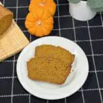 A freshly baked loaf of homemade pumpkin bread sliced to reveal its moist, golden-orange interior on a cutting board with little pumpkins.
