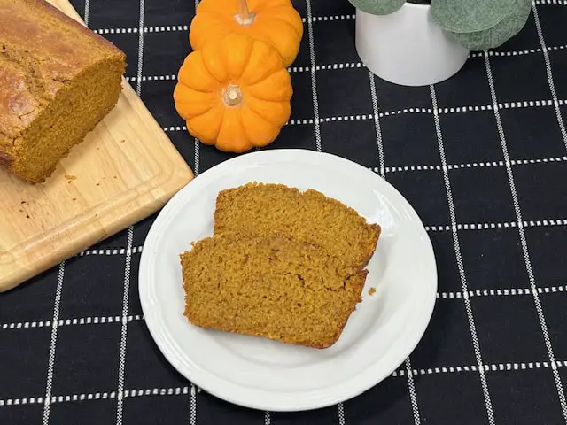 A freshly baked loaf of homemade pumpkin bread sliced to reveal its moist, golden-orange interior on a cutting board with little pumpkins.
