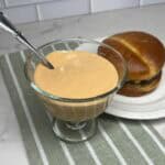 A small bowl of creamy homemade burger sauce with a spoon and a burger.
