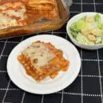 A slice of homemade grandma's lasagna with layers of melted cheese, meat sauce, and pasta, served on a white plate with fresh basil garnish.