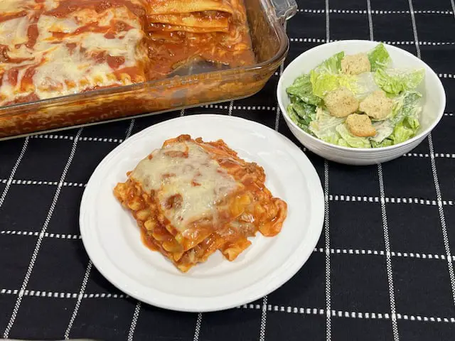 A slice of homemade grandma's lasagna with layers of melted cheese, meat sauce, and pasta, served on a white plate with fresh basil garnish.