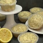 A batch of golden lemon poppy seed muffins with a light drizzle of lemon glaze, sitting on a white cake plate.