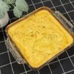 A steaming baking dish full of cheesy scalloped potatoes topped with parsley and bacon crumlbles