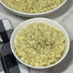 A bowl of creamy basil pesto mac and cheese with melted cheese. Topped with a bit of dried parsley.