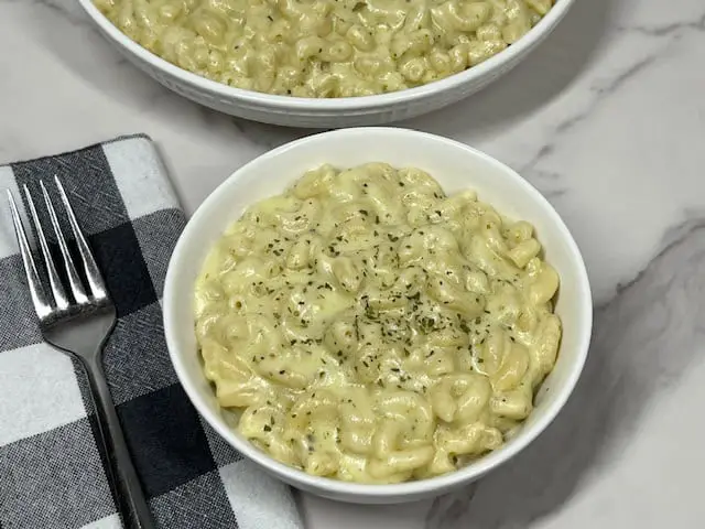 A bowl of creamy basil pesto mac and cheese with melted cheese. Topped with a bit of dried parsley.