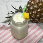 Creamy homemade pineapple freeze dessert beverage in a glass with a piece of pineapple for garnish.