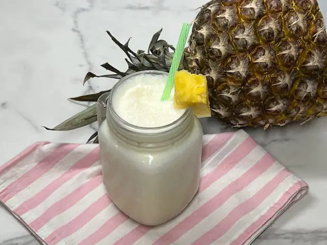 Creamy homemade pineapple freeze dessert beverage in a glass with a piece of pineapple for garnish.