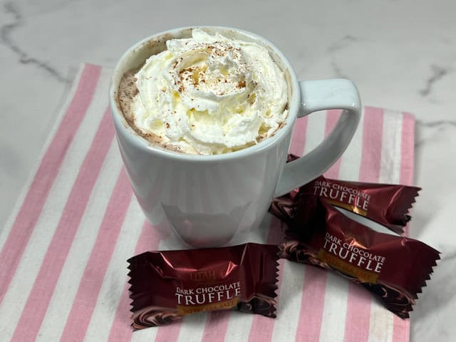 A steaming mug of dark chocolate sea salt hot cocoa, topped with whipped cream and sprinkled with cinnamon.