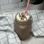 Frozen Hot Cocoa in a glass. with a straw, topped with whipping cream and chocolate curls.