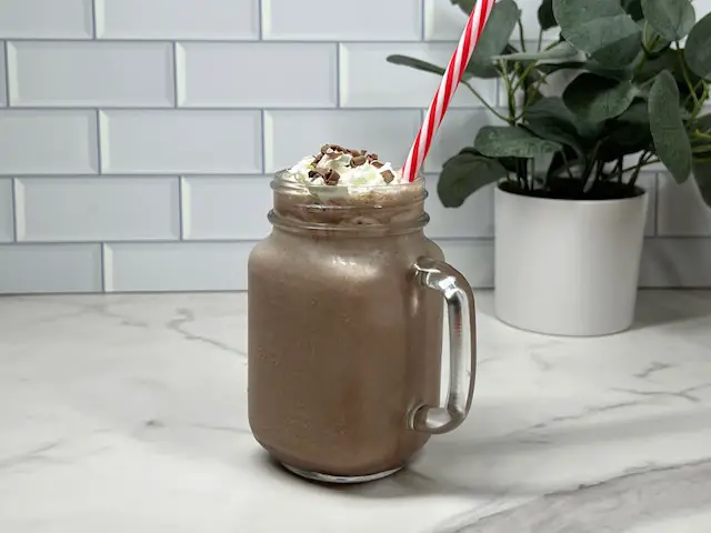 Frozen Hot Cocoa in a glass. with a straw, topped with whipping cream and chocolate curls.