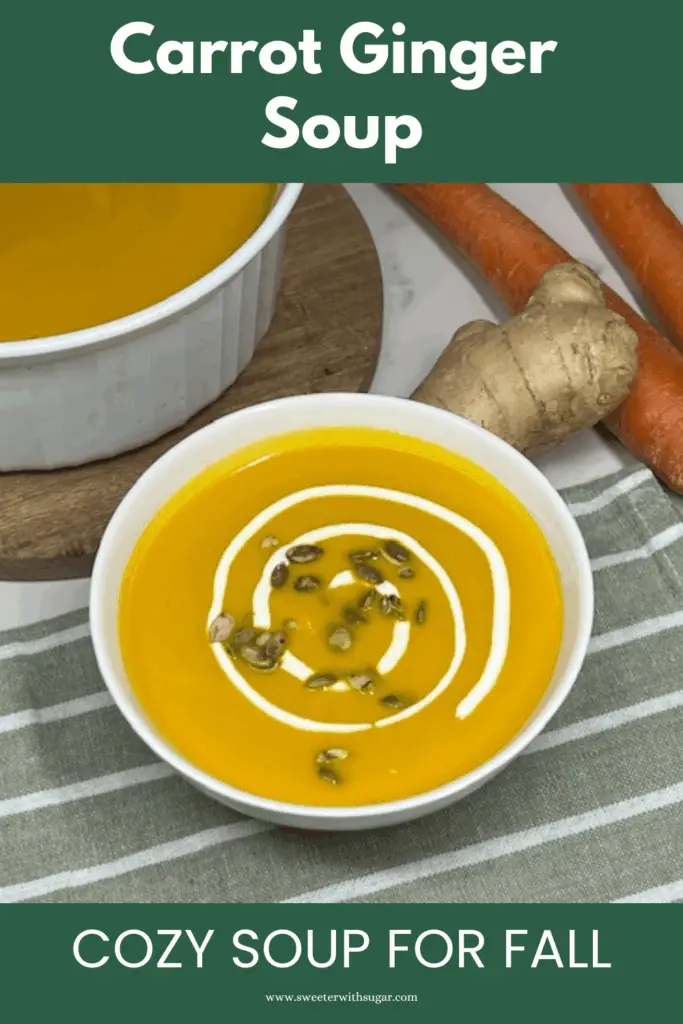 Bowl of smooth carrot ginger soup topped with sour cream and pumpkin seeds.